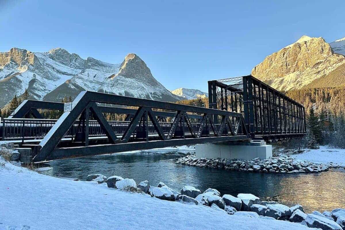 Canmore’s steel Engine Bridge over the Bow River, with snowy banks and mountains behind.