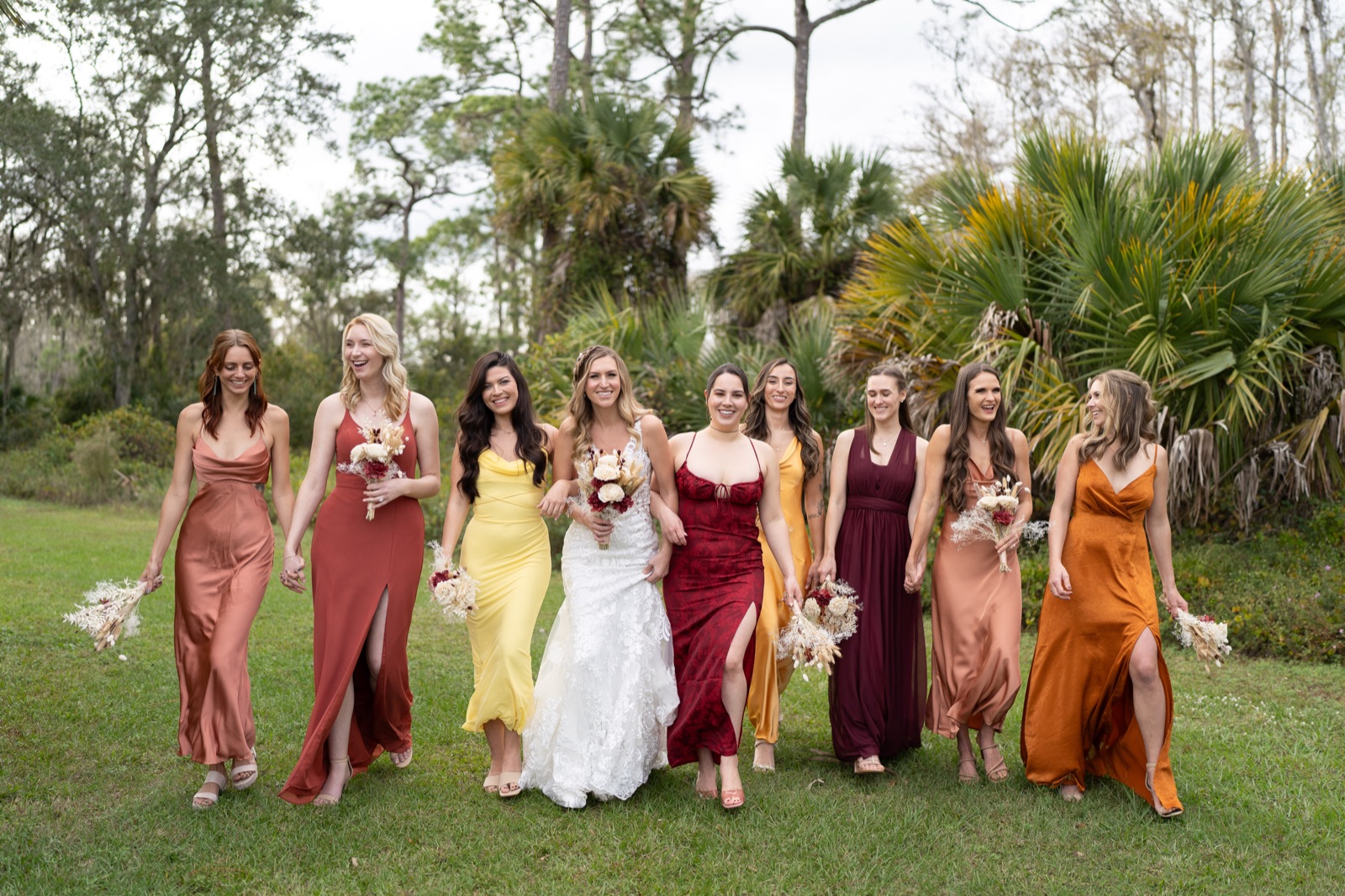 Bridesmaids walking with bride in warm autumn-toned dresses at Fort Myers barn wedding