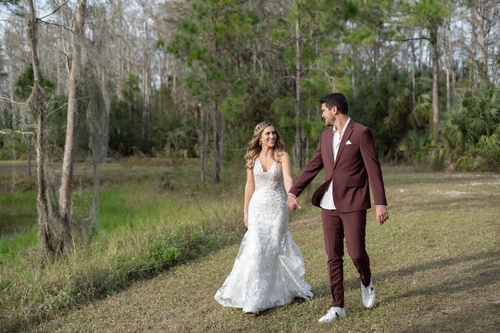 Kelli and Bradley walking hand in hand through the cypress trees and Spanish moss at Misty Morning Barn in Fort Myers, Florida