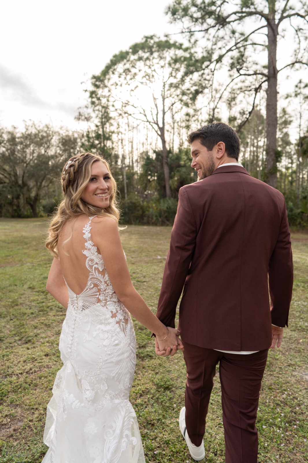 Kelli and Bradley walking hand in hand showing the back detail of bride's lace wedding dress at Misty Morning Barn