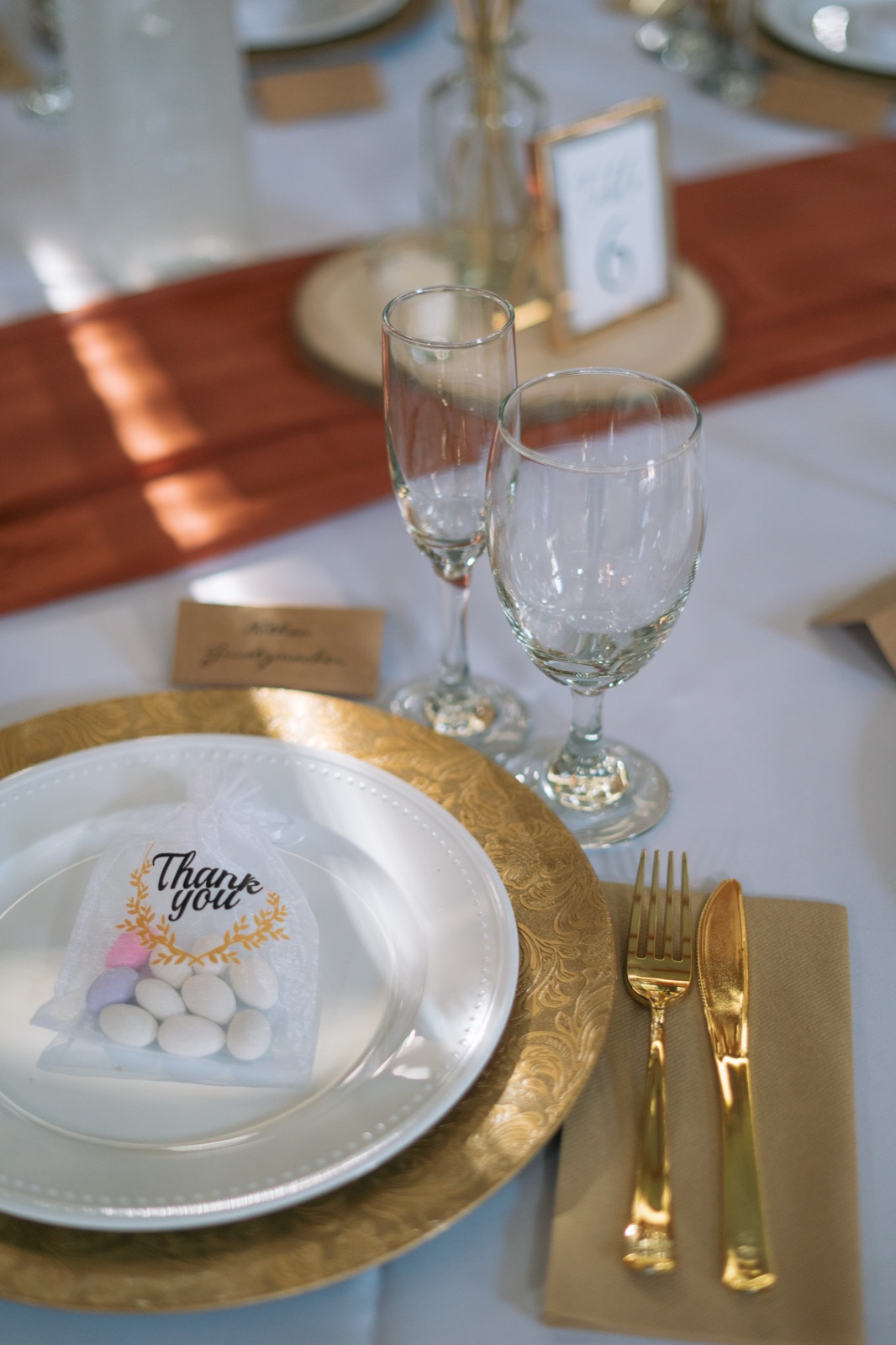 Gold charger place setting with thank you favor bag, gold flatware, and champagne flutes at Kelli and Bradley's Fort Myers barn wedding