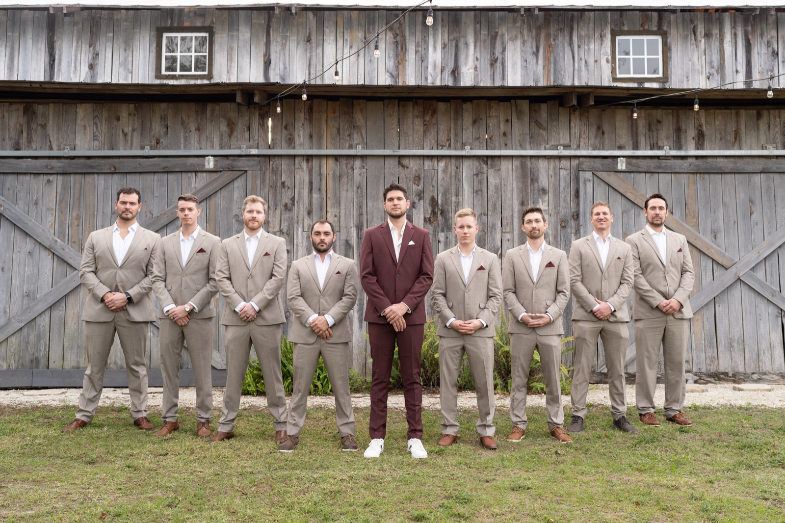 Groomsmen in tan suits with groom in burgundy suit standing in front of Misty Morning Barn
