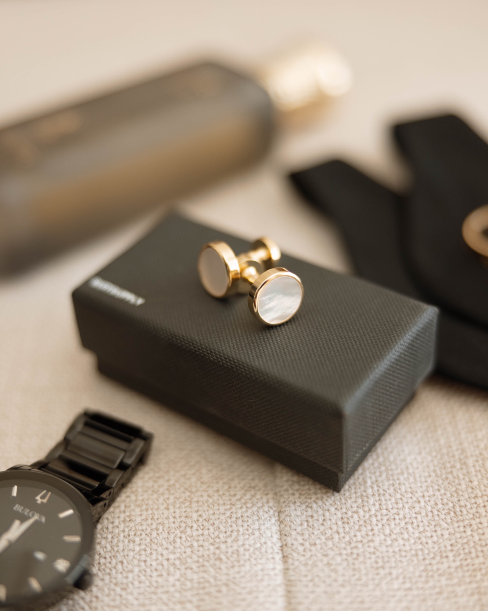 Gold cufflinks and a black watch beside the groom's cologne
