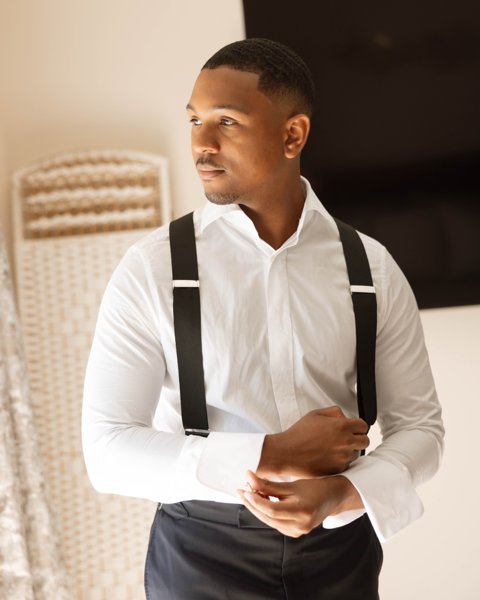 The groom fastening his cuff in suspenders and a white shirt