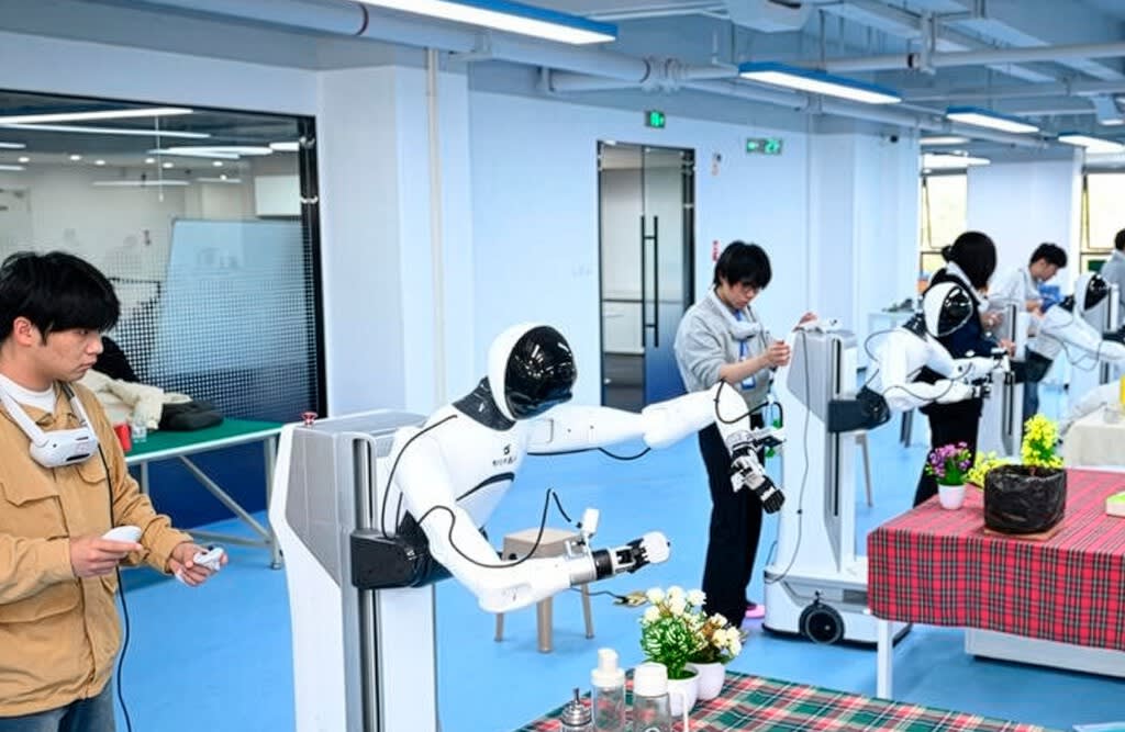 Un robot humanoide practicando una tarea simple en una fábrica de recogida de datos, con operarios humanos supervisando.