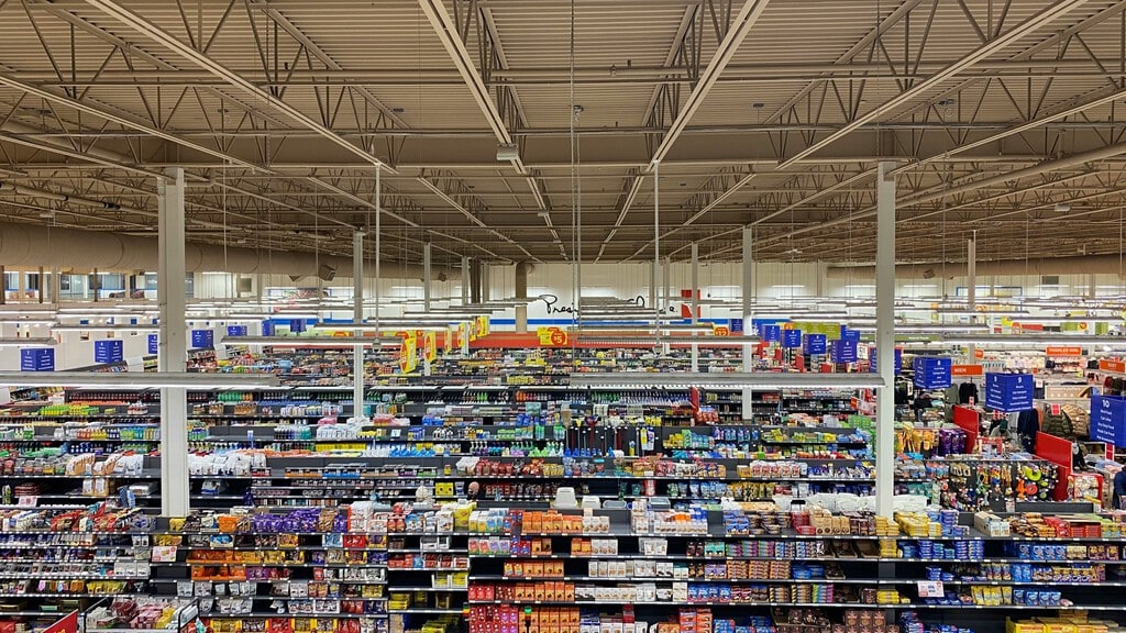 Interior de un supermercado moderno y luminoso con estantes bien surtidos, un cliente seleccionando productos.