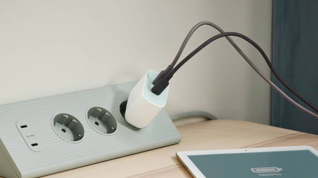 Un iPhone conectado a un cargador de pared moderno y potente, destacando su diseño elegante y la eficiencia de carga.