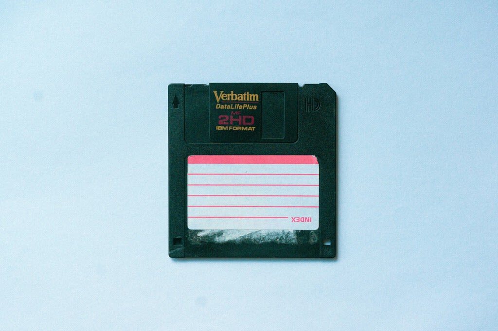 Un disquete de 3.5 pulgadas junto a un procesador de IA moderno, simbolizando la contraposición entre el software ligero y la era de la IA.