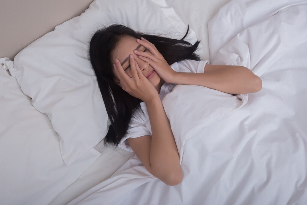 Persona levantándose de la cama en una habitación tenue, con una luz suave indicando un nuevo intento de dormir.