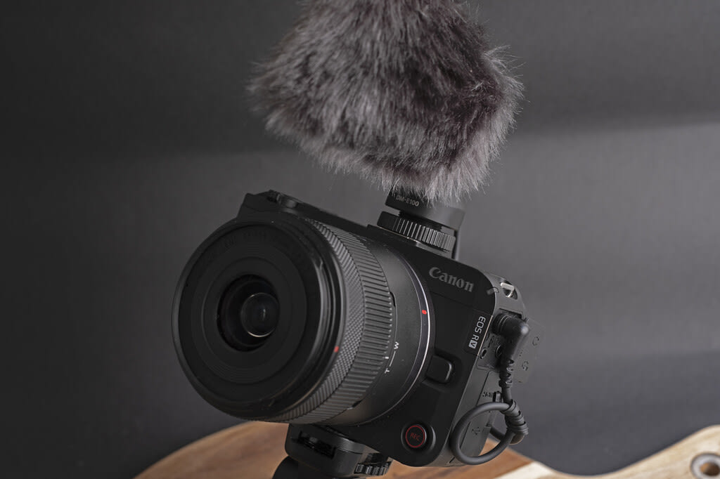 Canon EOS R50 V camera angled with its screen flipped out, showcasing its compact design and vlogging-ready features. A microphone is attached to the hot shoe.