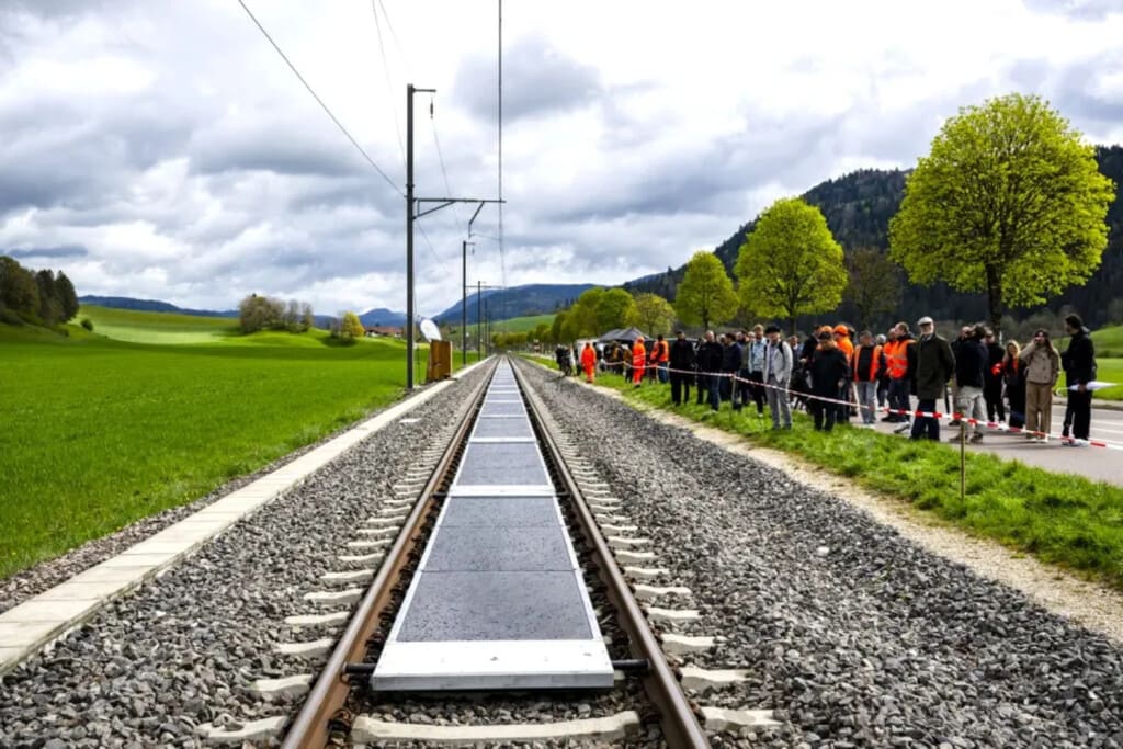 Paneles solares instalados entre las vías de un tren suizo bajo un cielo despejado.