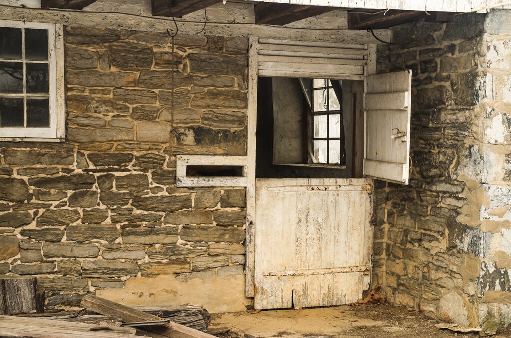 Una puerta de madera antigua partida por la mitad, con la hoja superior abierta y la inferior cerrada, en un entorno rural.