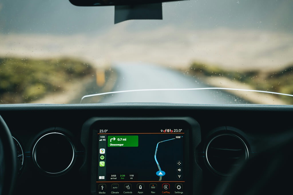 Primer plano de un adaptador CarPlay inalámbrico conectado a un puerto USB en el salpicadero de un coche moderno, con el iPhone mostrando la interfaz de CarPlay en la pantalla del vehículo.