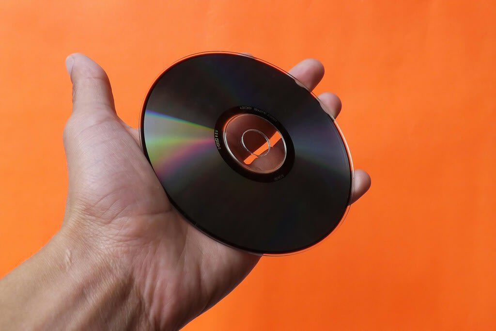 Un primer plano de varios CDs apilados, con uno de ellos ligeramente inclinado, destacando su superficie brillante bajo una luz suave y controlada.