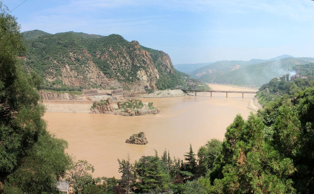 Panorámica del Río Amarillo en China mostrando cambios en su coloración, con áreas reforestadas y presas visibles.