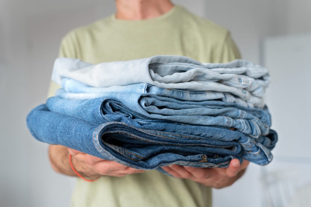 Pantalones vaqueros de color azul oscuro doblados cuidadosamente sobre una superficie de madera clara, con una luz suave que resalta la textura del tejido.
