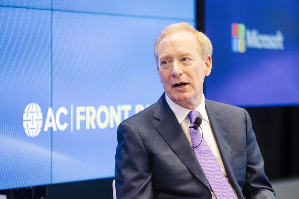 Brad Smith, presidente de Microsoft, hablando en un podio con un fondo tecnológico abstracto.