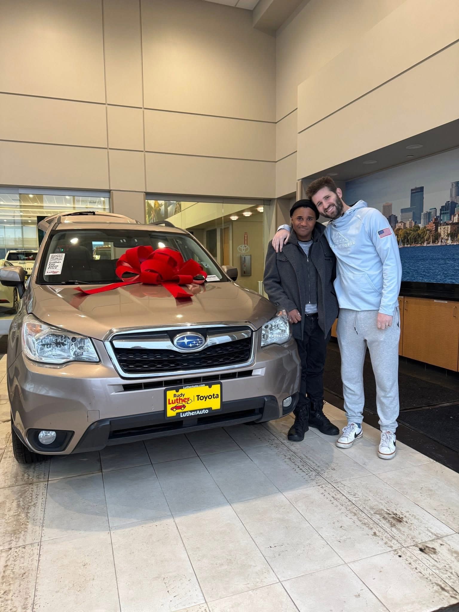 Josh Liljenquist standing with a recipient beside a gifted Subaru during a community support project.