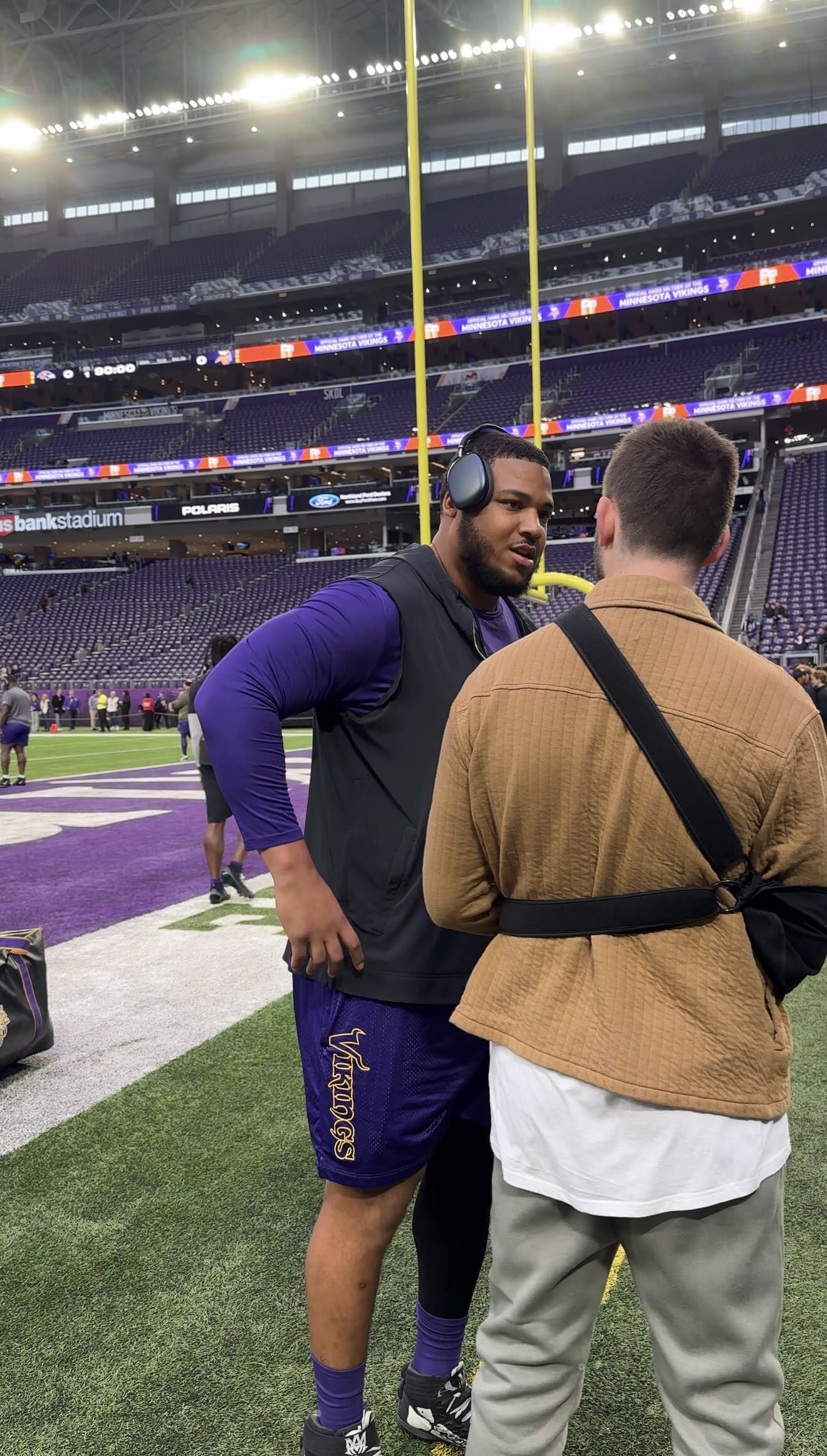 Creator speaking with a Minnesota Vikings player on the field at U.S. Bank Stadium during a community game-day experience.