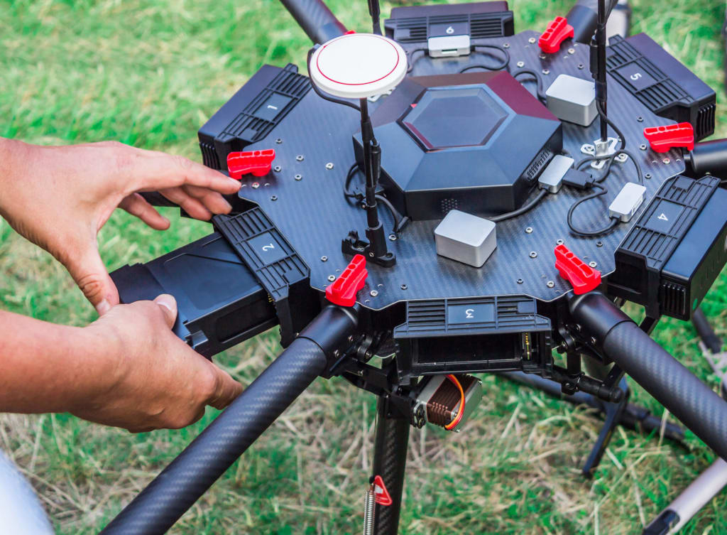 A person is handling a hexacopter drone with various components and numbered sections, adjusting parts on the grass.