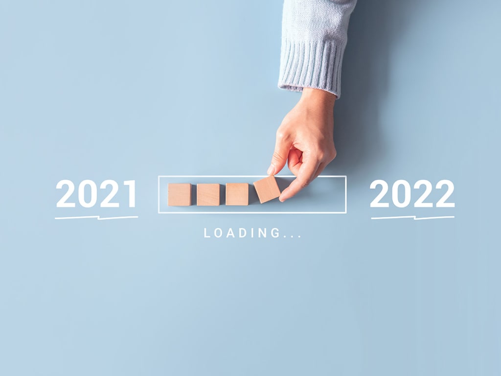 A hand places wooden blocks, forming a partial progress bar between "2021" and "2022" with the word "loading" below the bar, symbolizing the transition from one year to the next.