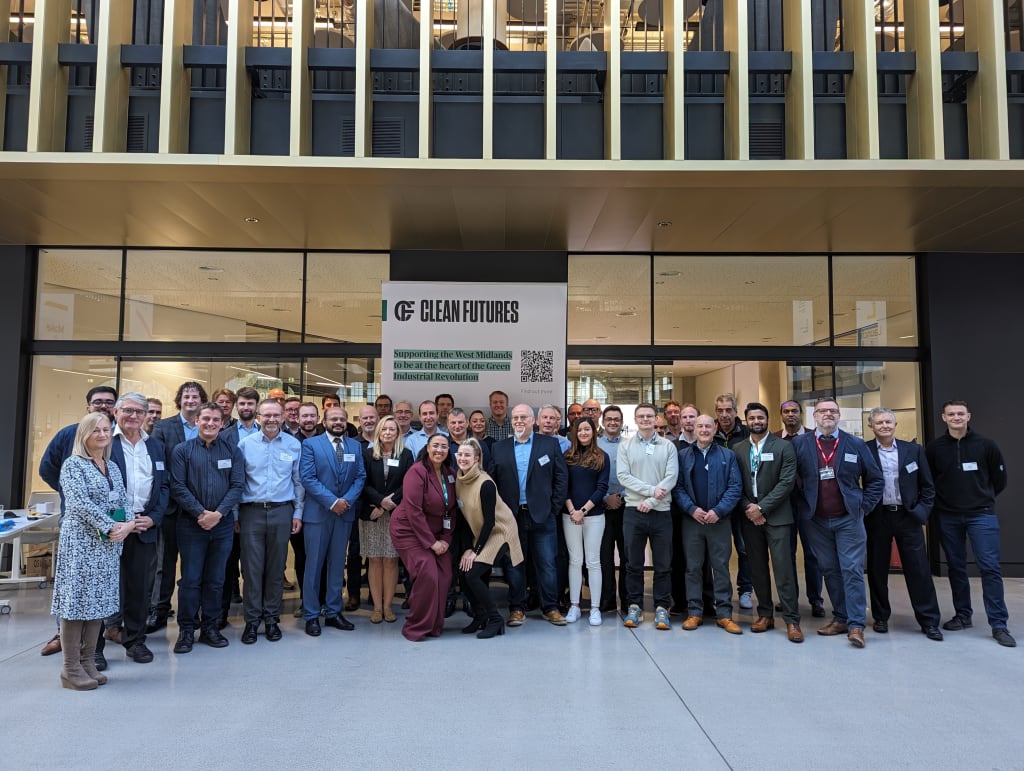 A large group of people stands in front of a "Clean Futures Accelerator" sign, posing for a group photo inside a modern building.