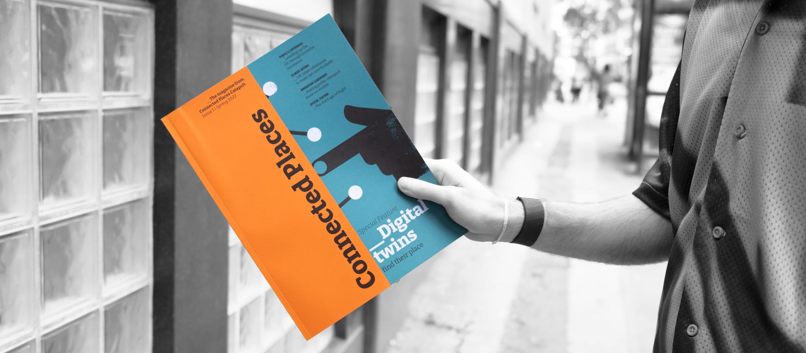 A person holds an orange and blue book titled "Connected Places: Digital twins" in a bustling city street, emphasizing the concept of connected places.