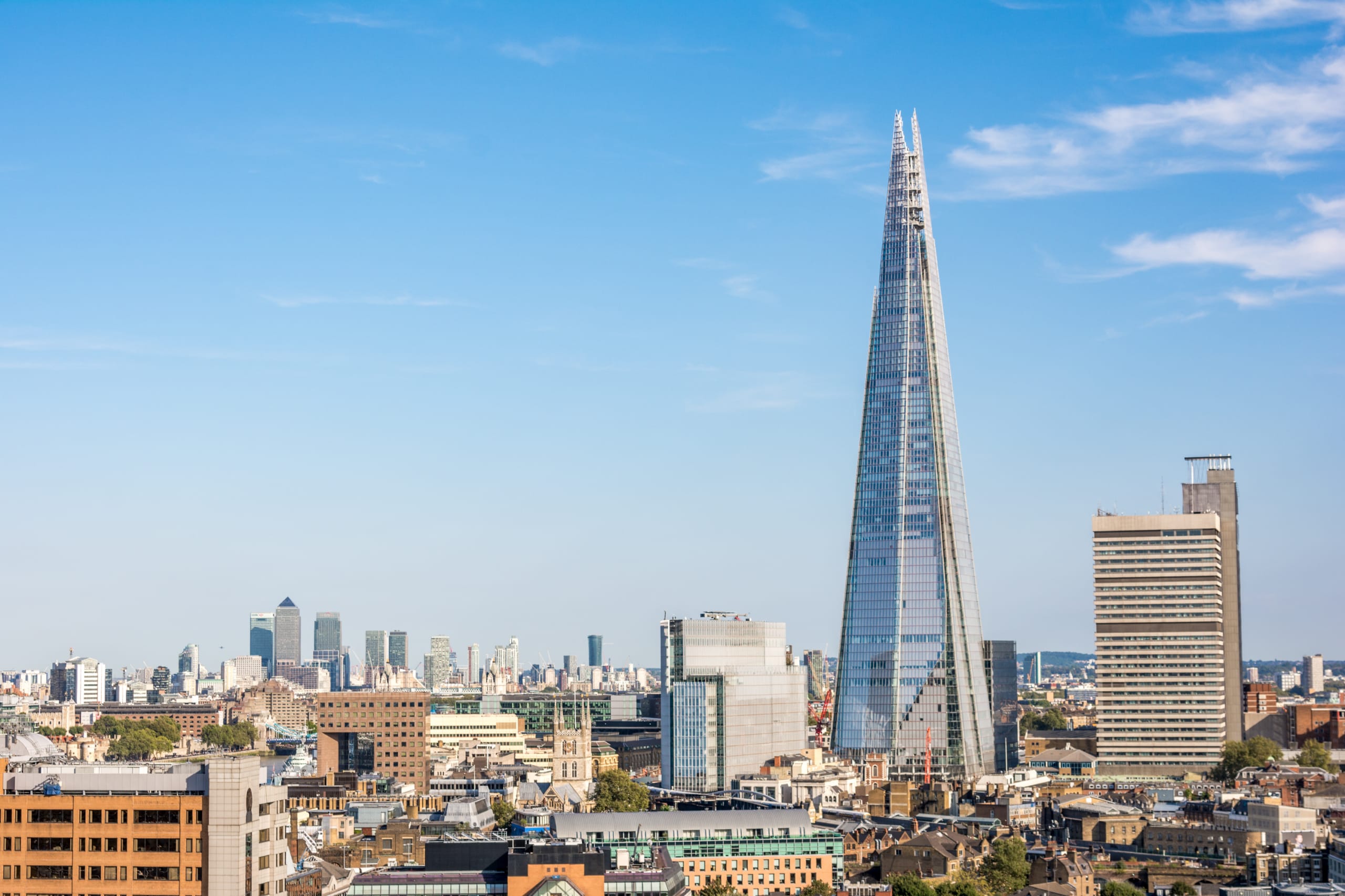 Skyline featuring The Shard, a tall skyscraper with a pointed top, surrounded by various buildings in central London under a clear blue sky.