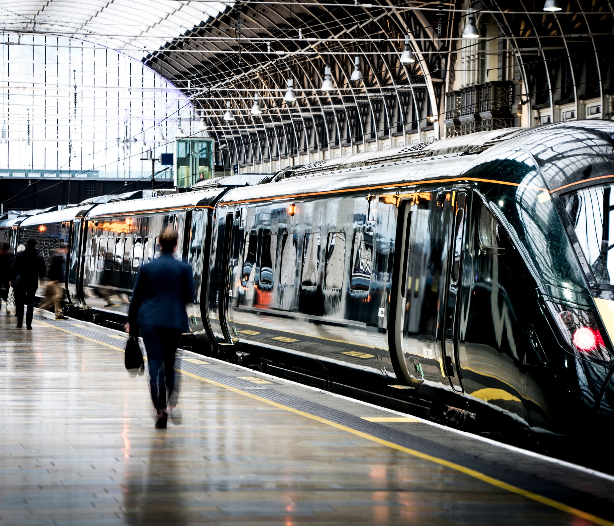 A person walks along the platform beside a modern passenger train at a station with an arched glass roof, embodying a future rail experience.