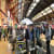 A busy train station with people walking through ticket barriers and along the platform next to a stationary train under the large, arched roof of Bristol Temple Meads.