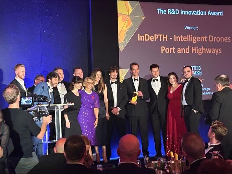 A group of people in formal attire stands on a stage holding an award. A large screen behind them displays the text "The R&D Innovation Award" and "Winner: InDePTH - Intelligent Drones Port and Highways.