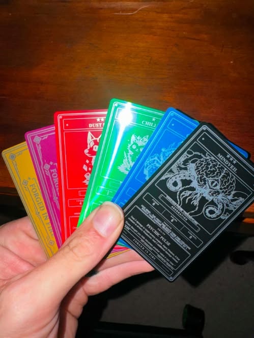 Forged in Fire metal cards displayed in black, red, blue, green, purple, and gold finishes