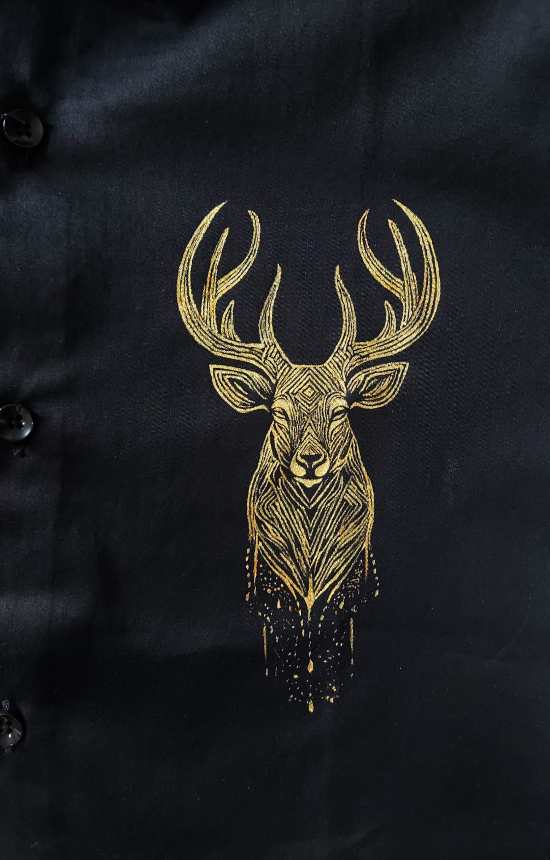 Intricate golden stag head painted with fine geometric line art details on a black fabric background.