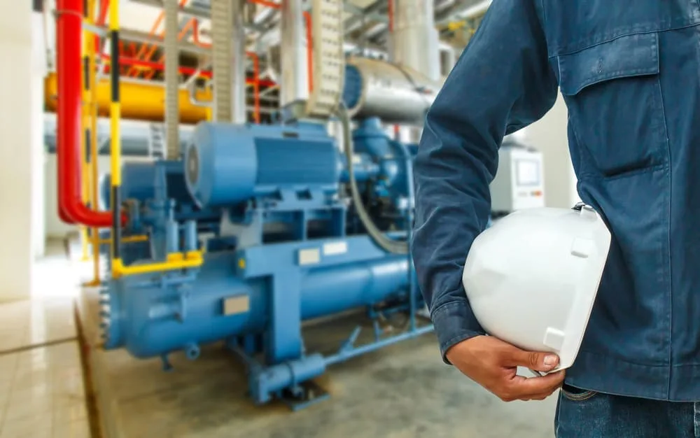 Primer plano una persona con un casco de seguridad industrial, al fondo maquinaria industrial