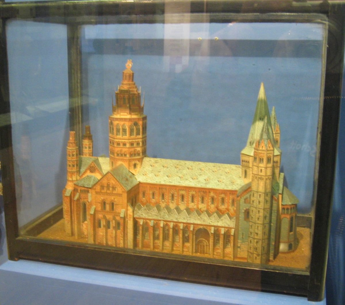 A detailed cardboard model of Mainz Cathedral, with towers and coloured roofs, inside a glass display case.