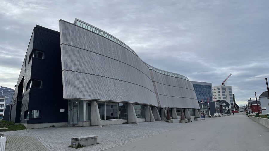 The curved, timber-clad facade of the Katuaq cultural center in Nuuk on an overcast day, with a paved street running alongside.