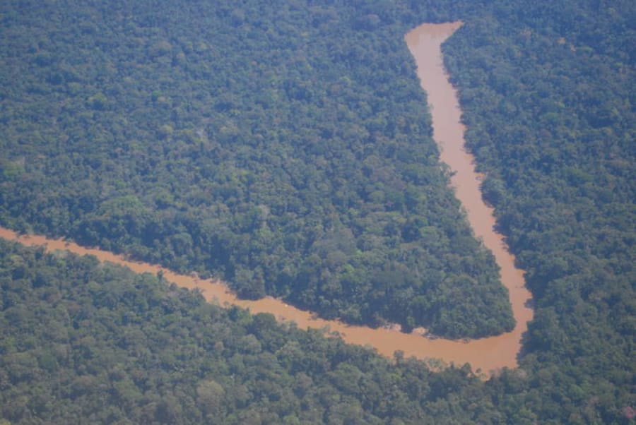 A brown Amazon river curving between banks of dense green rainforest under a cloudy sky.