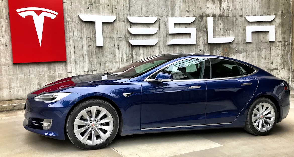 Blue electric vehicle parked in front of Tesla dealership sign