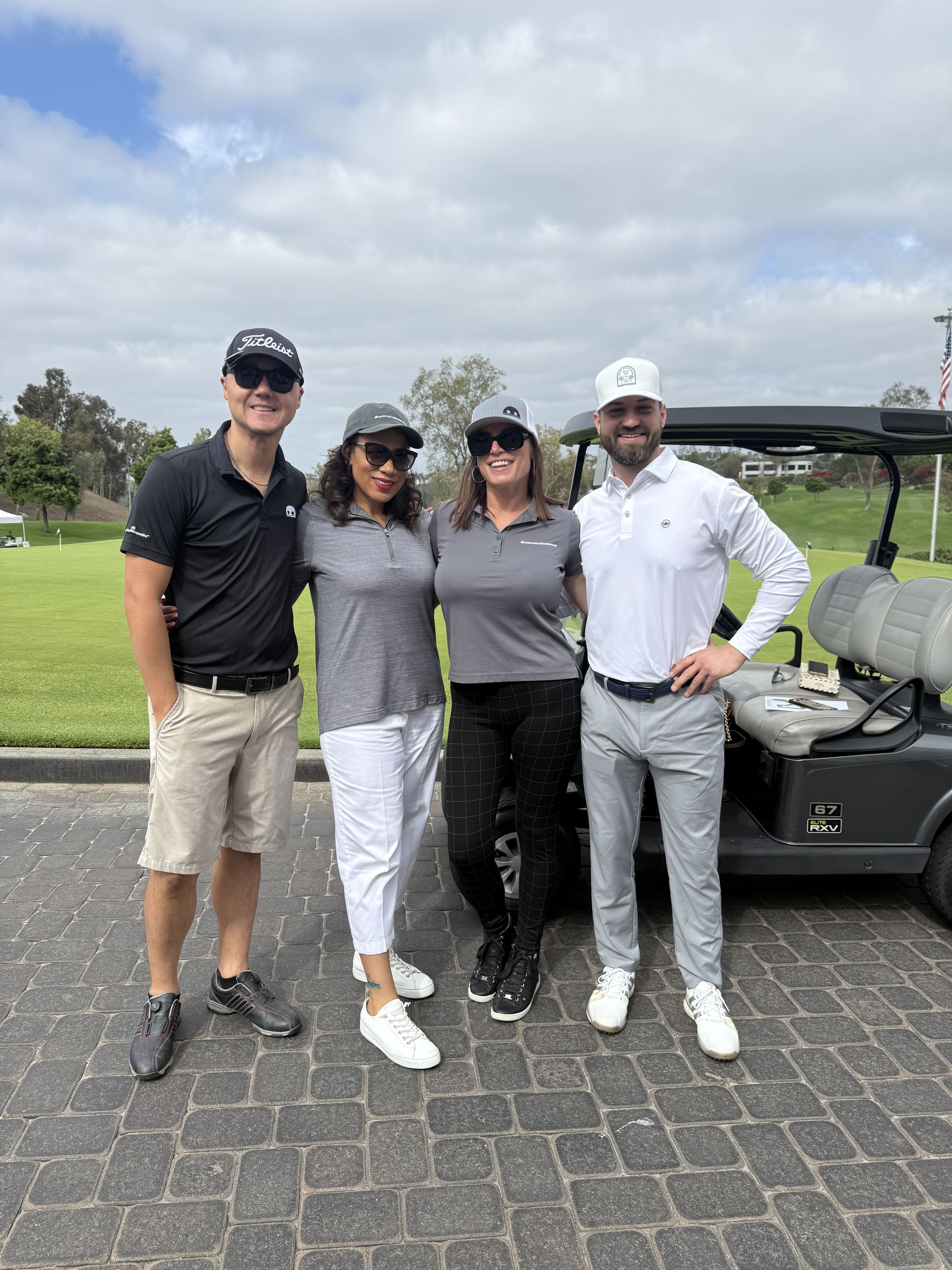 Four Masterminds arm-in-arm in golf attire in front of a golf cart and golf course.