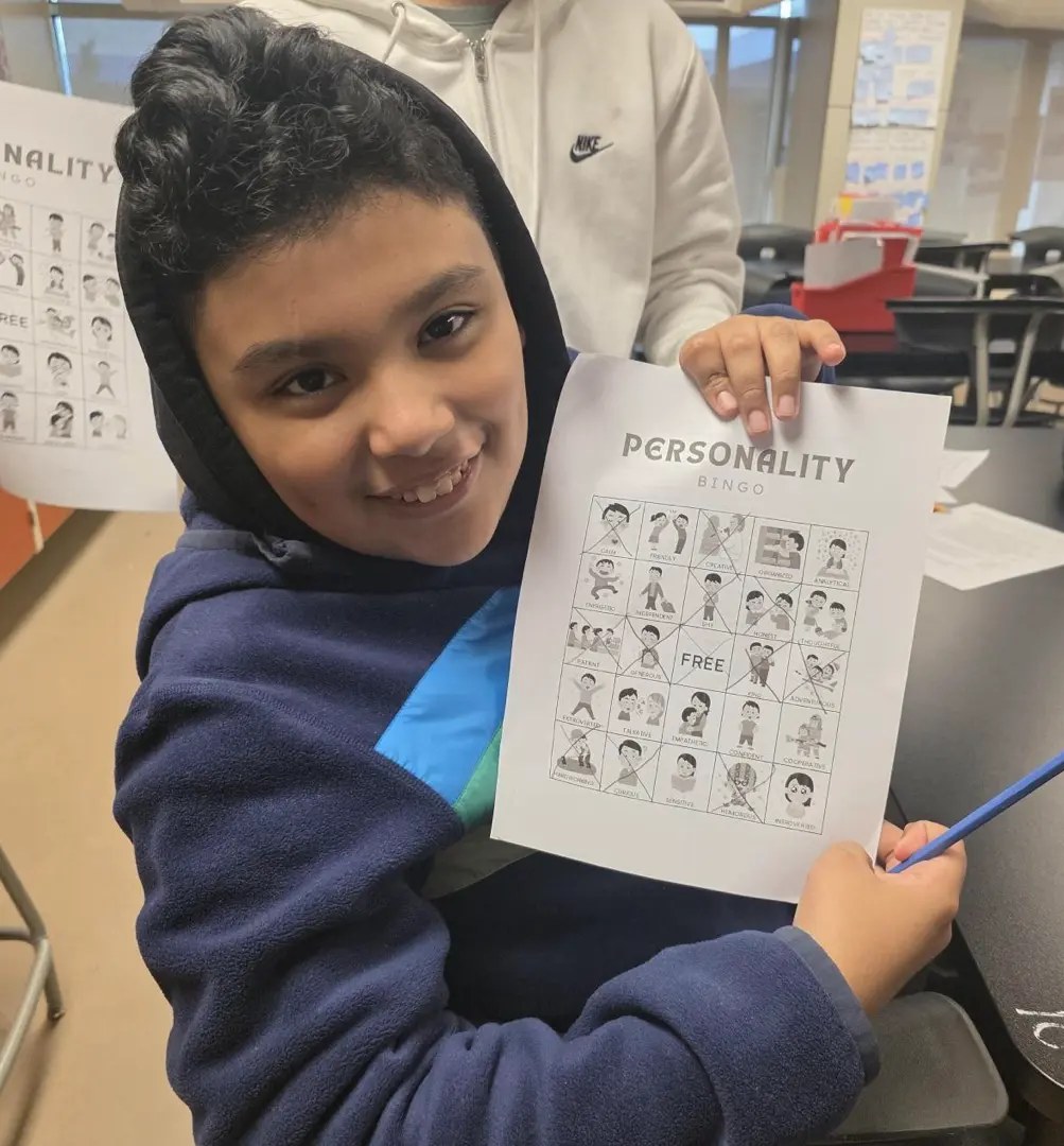 A child wearing a blue hoodie holds up a piece of paper