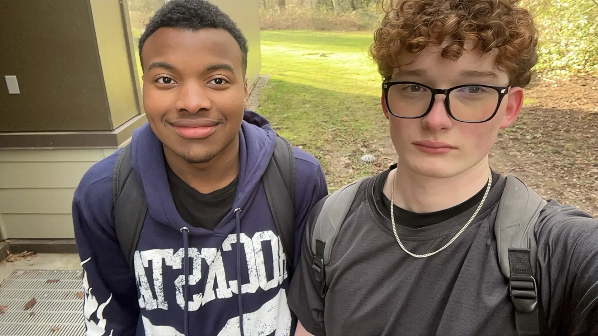 From left: a boy wearing a blue hoodie with white lettering and a boy wearing glasses and a grey shirt