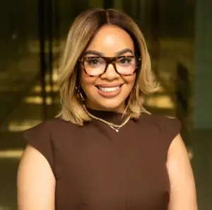 Woman wearing a brown shirt and glasses smiles at the camera
