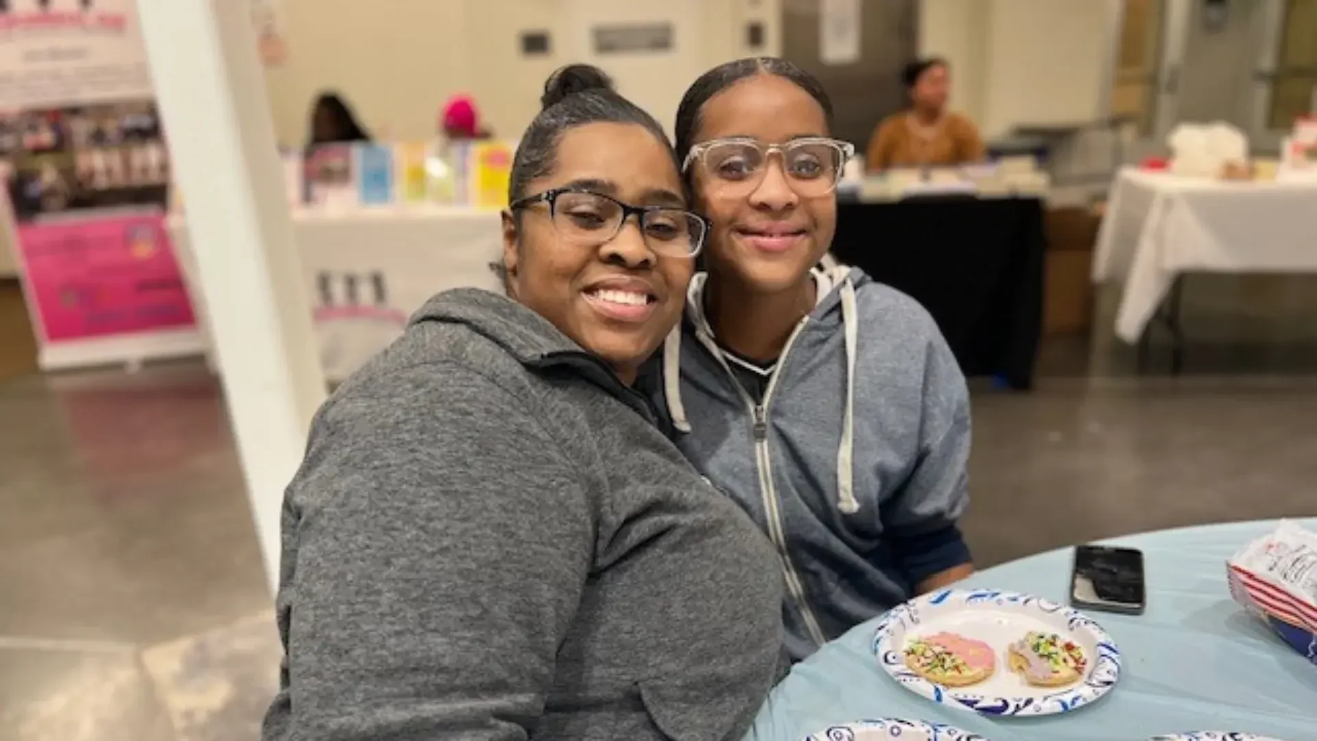 A woman wearing a grey shirt smiles with a girl wearing a grey shirt