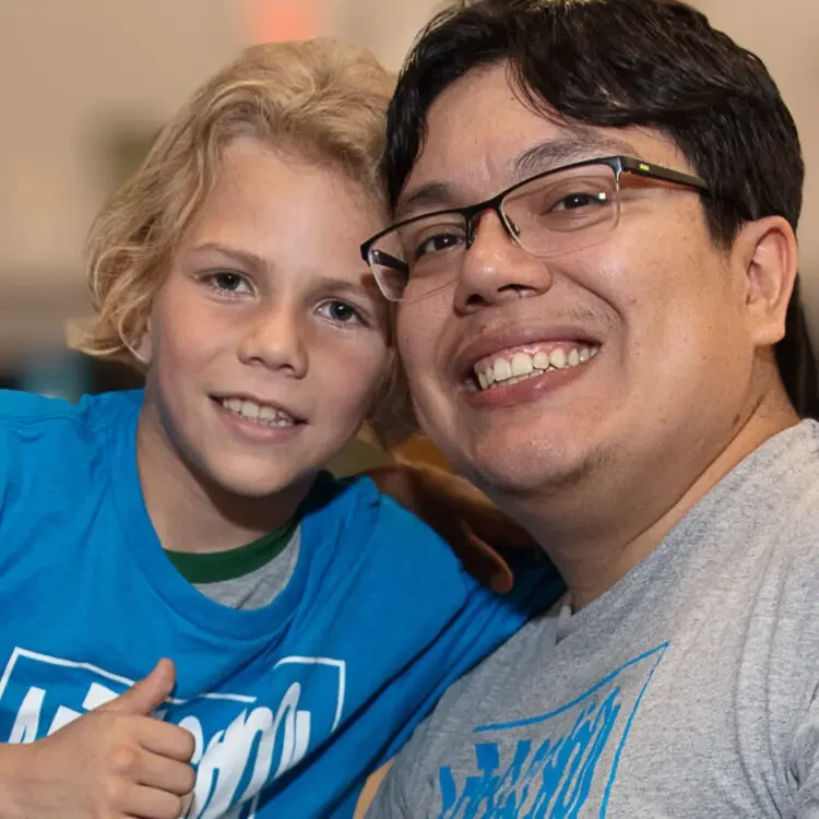 A man with glasses and a grey shirt and a student with a blue shirt giving a thumbs up