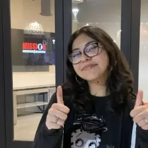 Student wearing glasses gives a thumbs up to the camera