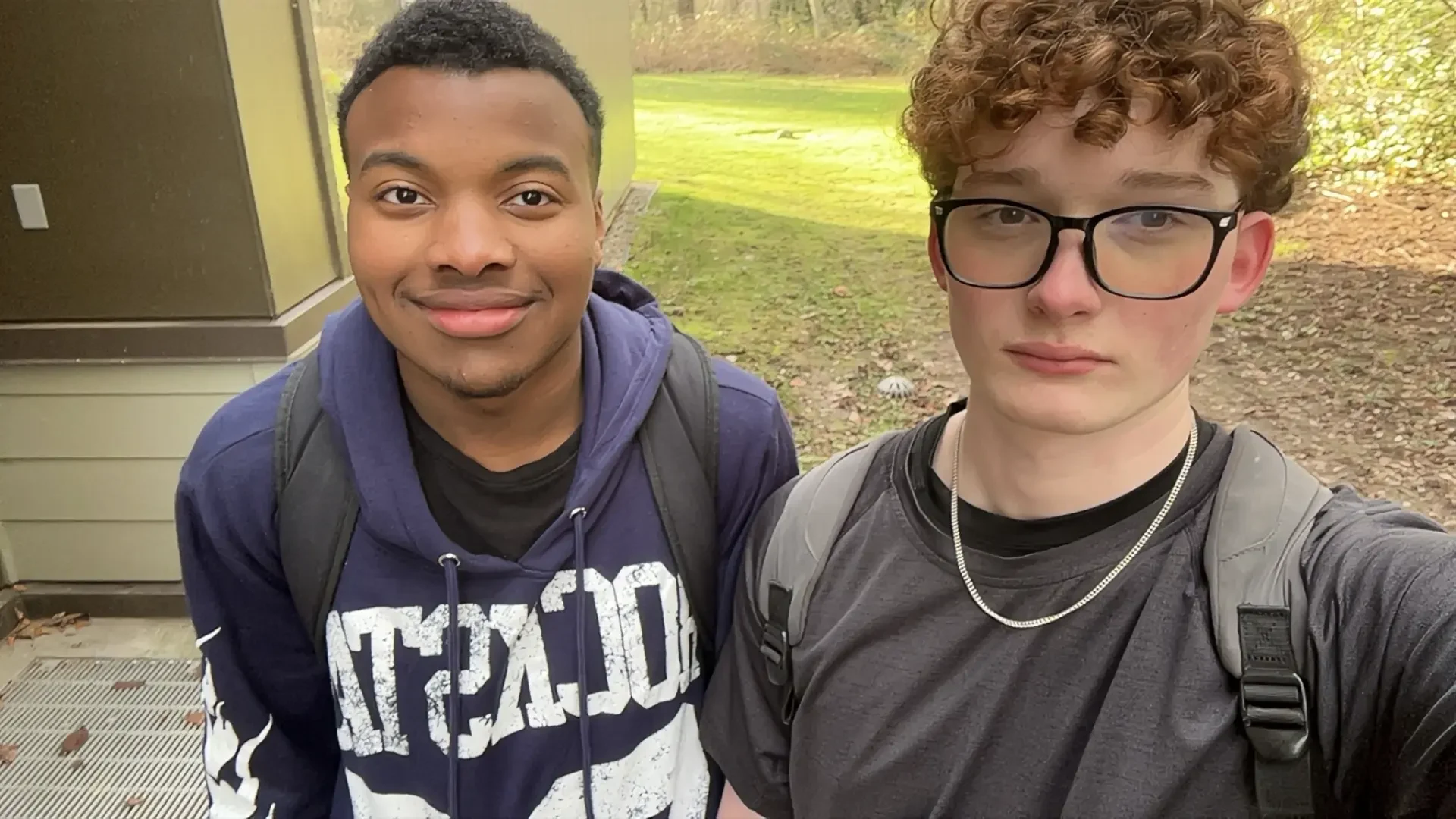 From left: a boy wearing a blue hoodie with white lettering and a boy wearing glasses and a grey shirt