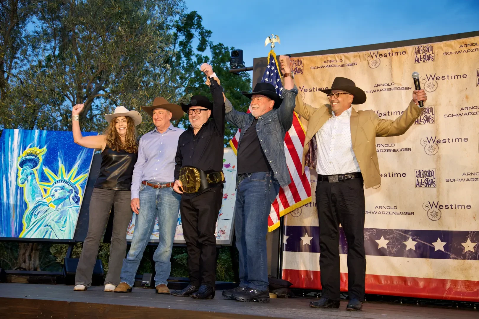 Five people on a stage raise their arms in celebration.