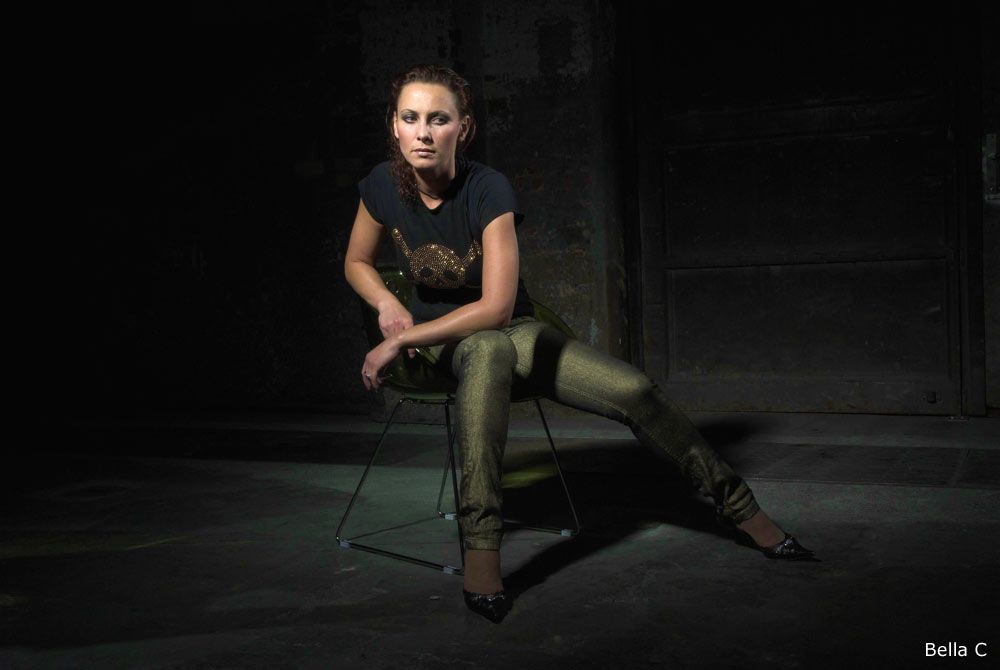 Bella C. with tight trousers, black shirt, sitting