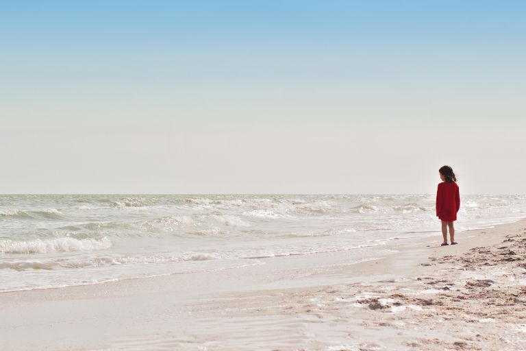 Youn girl at the beach looking into the sea and horizon