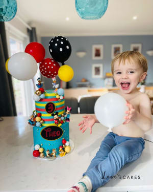 Celebration cake: A little boy is sitting on a table with balloons